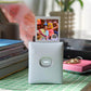 Fujifilm Instax Square Link printer in light blue placed on a tiled desk, printing a fun birthday photo with party hats and QR code. Ideal for home use, gifting, or creative projects.