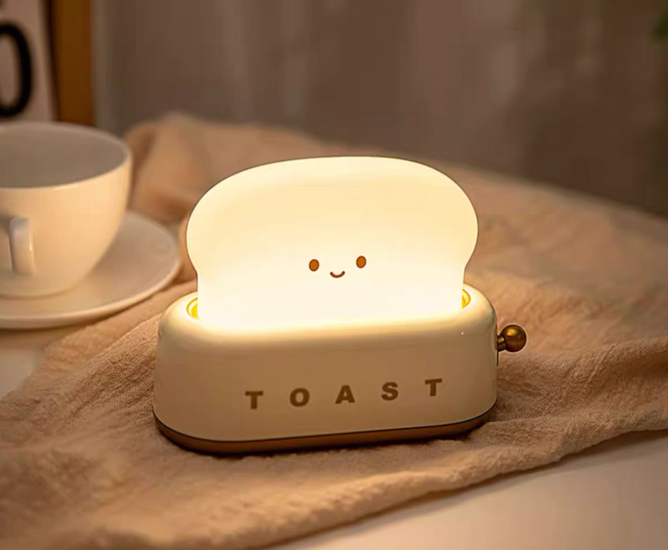 White toaster night light glowing on bedside next to teacup and saucer for cosy bedroom ambience