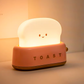 Pink toaster-shaped night light lit on desk against neutral wall showing rosy colour option and warm bedside glow
