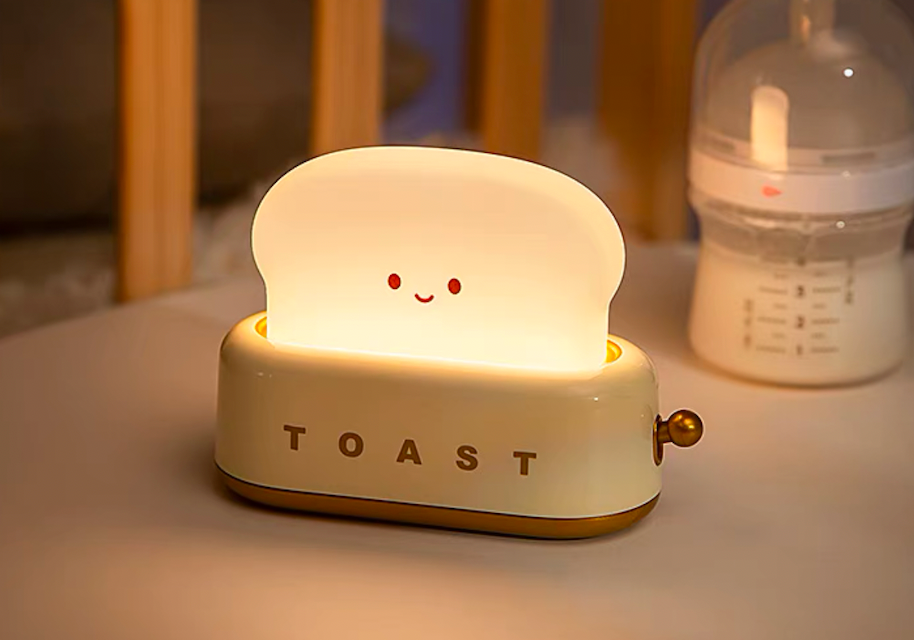 White toaster night light glowing on nursery dresser beside baby feeding bottle showing gentle bedside lamp glow